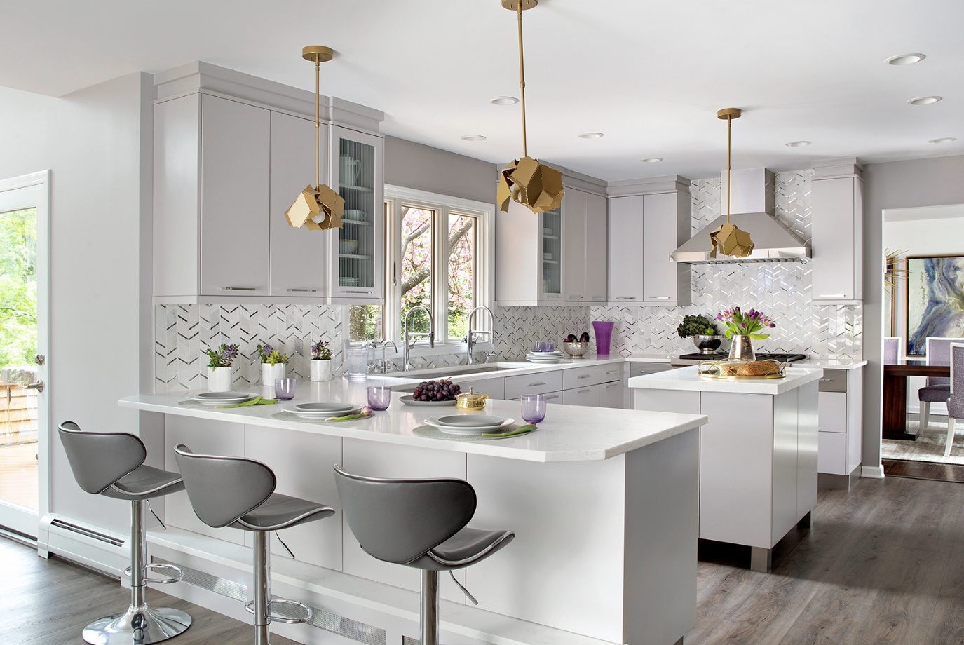 The wood-look vinyl tile flooring, in shades of cool gray and warm tan, is foot-friendly and durable. The stone and mirror chevron mosaic backsplash draws the eye, seamlessly adding elegance and continuity to the room’s design