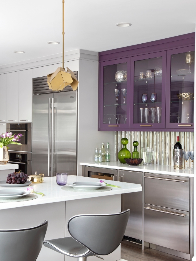 The eye is immediately drawn to the vibrant purple and stainless front cabinetry and appliances in the bar area. This serves as a striking focal point while seamlessly connecting the adjacent living and dining spaces to the kitchen. The thoughtful incorporation of gold metallics adds warmth, and elevates the design.